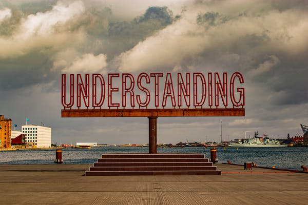 This image is of a small podium with steps and at the top of the podium, there is a thick rod standing vertically supporting a horizontal metal rod with the word " Understanding" soldered onto it.