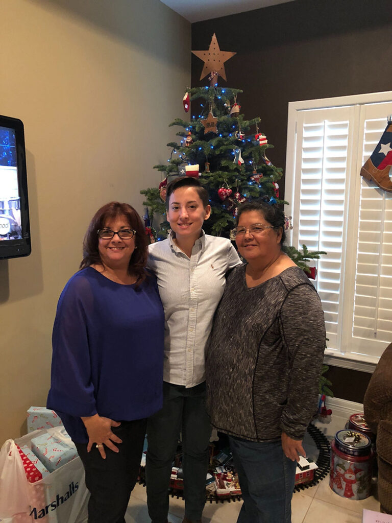 This image shows a person named Diego Guerra standing and two other women standing with a decorated Christmas tree in the background. Diego Guerra is wearing a white shirt.