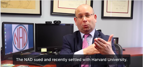 This image is of NAD's CEO, Howard A. Rosenblum sitting in front of the camera gesturing in sign language. There is a hovering text on the image which reads as " The NAD sued and recently settled with Harward University"