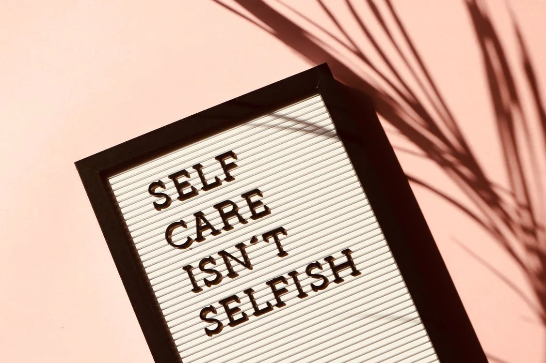 This image looks like a tilted frame on which there is written: " SELF CARE ISN'T SELFISH". The background has a peach color look to it.