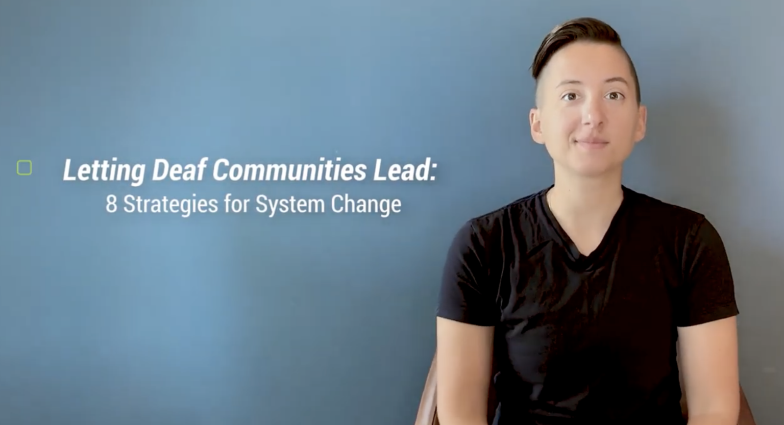 This image has a person sitting on a chair. The background is a blue color. There are some sentences on the screen which read " Letting Deaf Communities Lead: 8 Strategies for System Change"