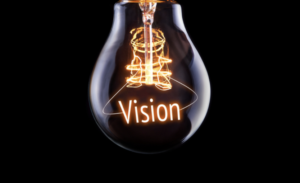 This image shows a filament bulb and the word " Vision" illuminating. The background is pitch black