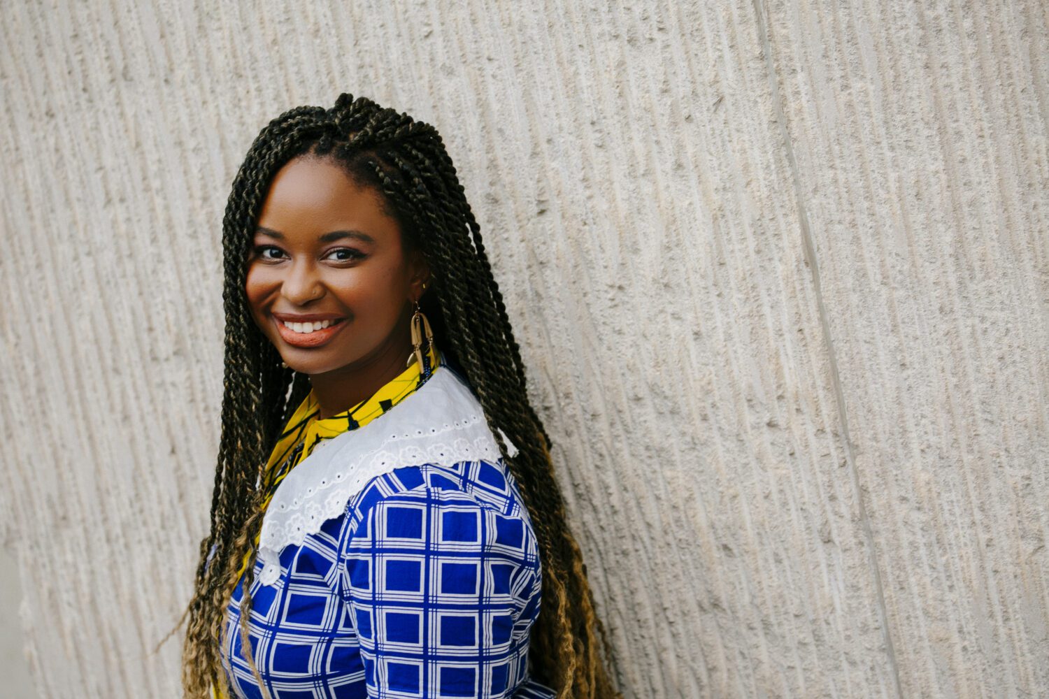 A person in black and yellow tipped dreadlocks in a blue blouse smiling for a photo.