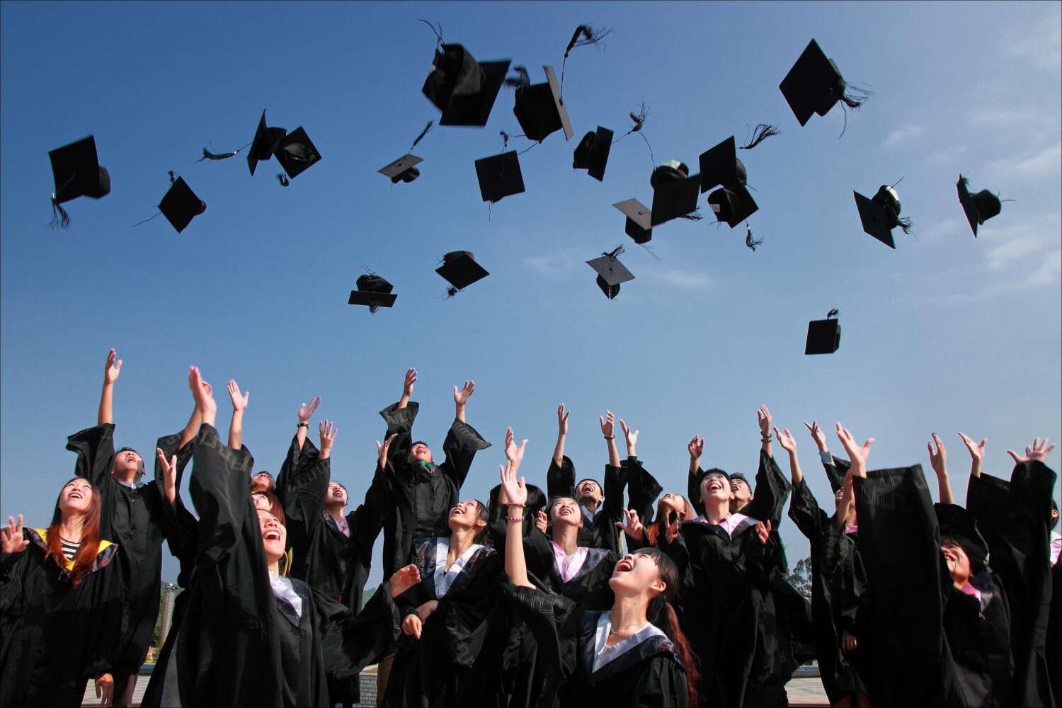 This image shows around fifteen to twenty students celebrating their graduation by throwing their graduation caps in the air.