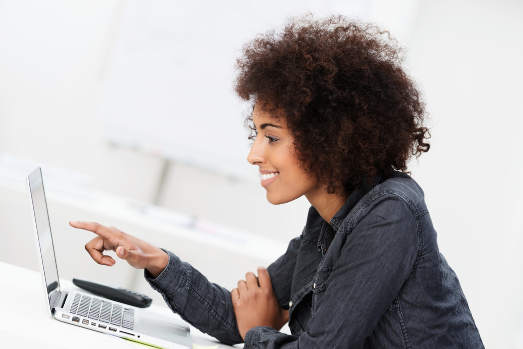 This image shows a side profile of a woman looking at the laptop screen. She appears to be smiling and has one hand pointing towards the screen. She has curly hair.