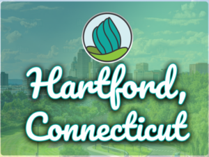 This image shows greenery and trees with tall buildings in the background. In the top center, there is the logo of NDC and below there is a text " Hartford Connecticut "