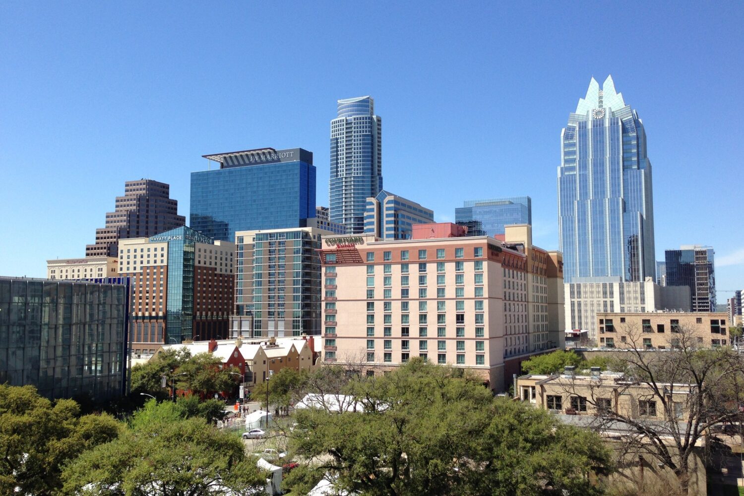 This is a rectangular image showing concrete buildings under a vibrant blue sky in Austin, Texas, United States. The modern architecture stands tall against the backdrop of the clear sky, creating a striking contrast. The scene portrays a sunny day with a sense of urbanity and architectural beauty