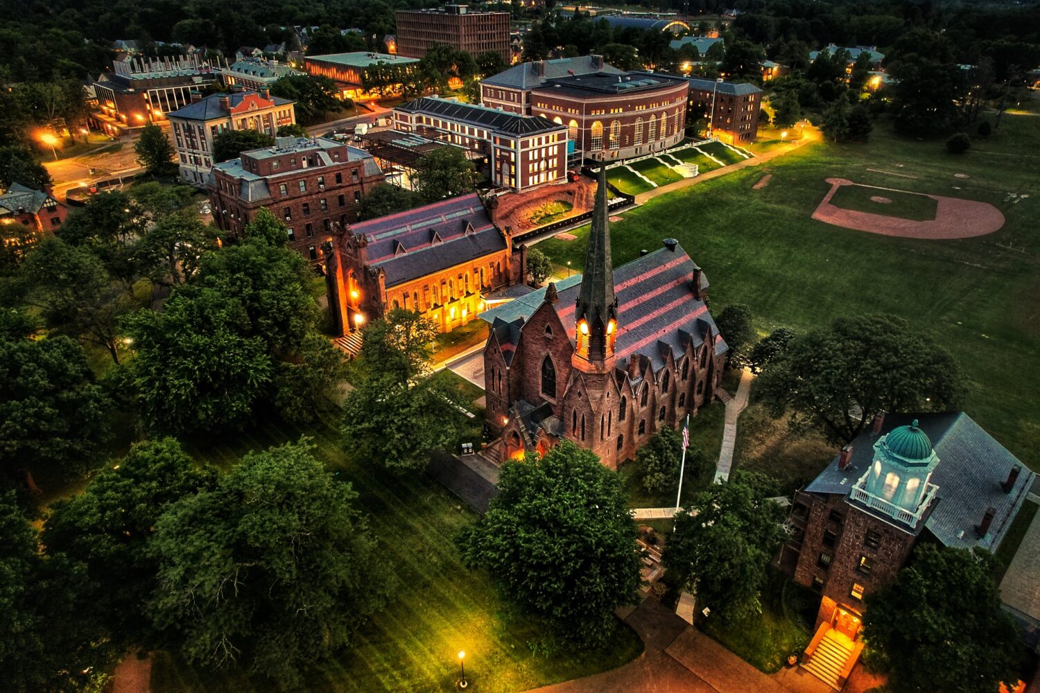 This is a large rectangular image of A serene and solemn Memorial Chapel illuminated by soft lighting at night. The chapel stands tall with its architectural features visible, including arched windows and a prominent spire. The surrounding area appears calm and peaceful, creating a reflective atmosphere