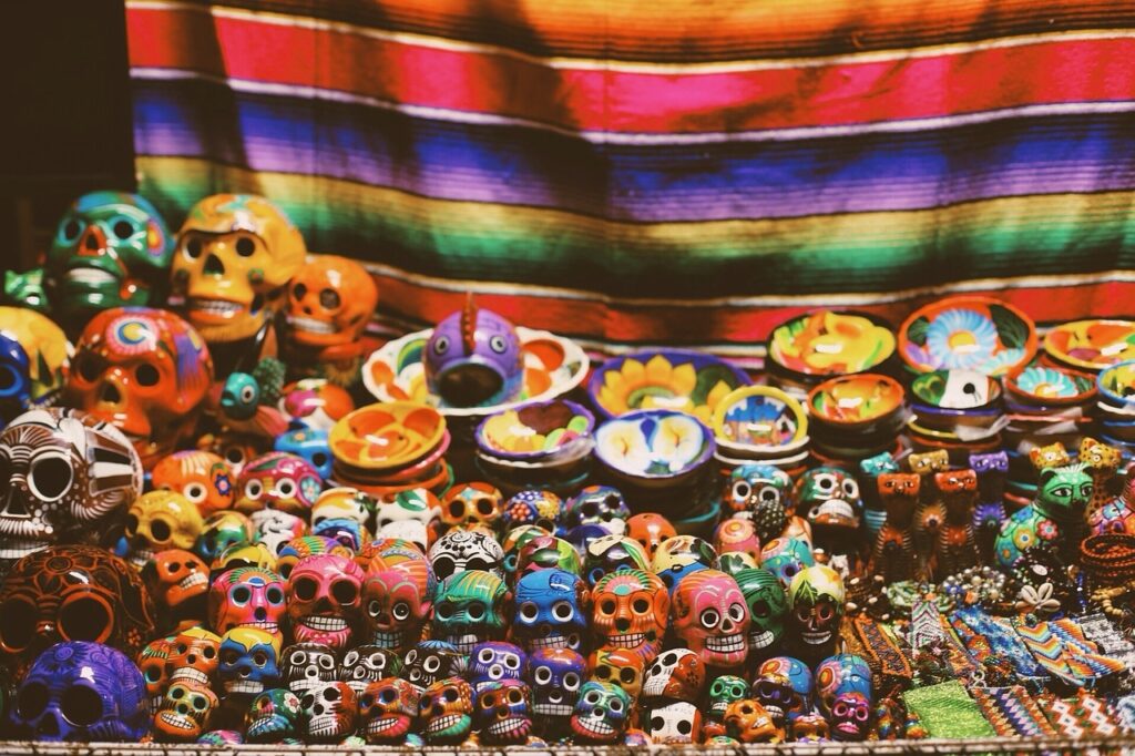 This is a rectangular image depicting a market scene during the Day of the Dead celebration, showcasing a variety of skull art. The artwork features skulls in different shapes and colors, representing the vibrant and creative spirit of the event. The intricate designs and vivid hues add a festive and cultural touch to the atmosphere.