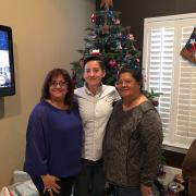 Diego Guerra, a Mexican-American wearing a white shirt stands between two Mexican-American women with a Christmas tree in the background.