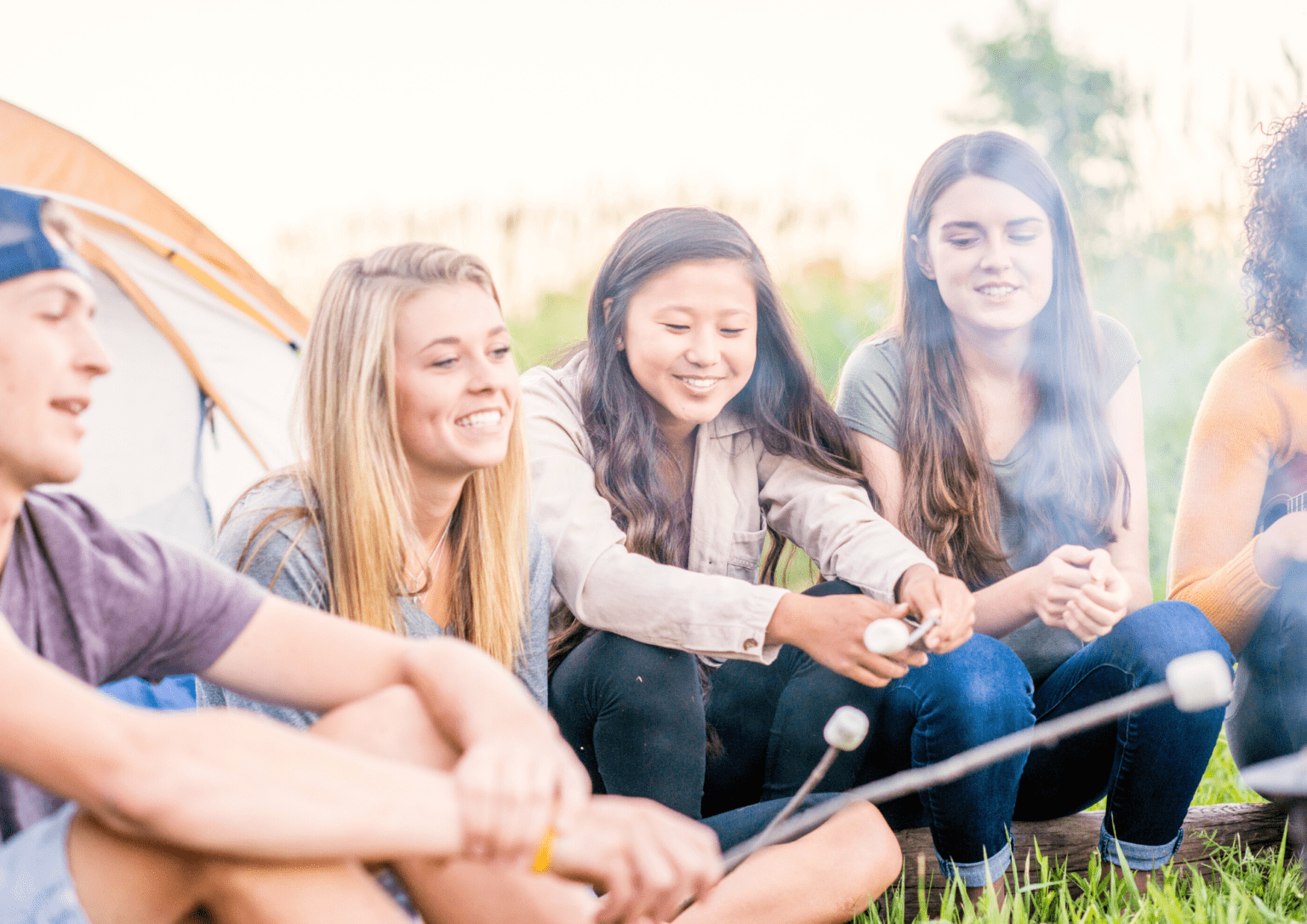 The image shows a group of people smiling sitting outdoors roasting marshmallows.