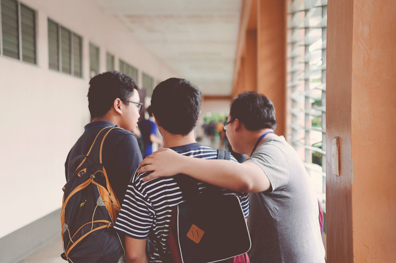 This image shows a corridor area of a school or educational institution. Three young boys appear to be talking with each other. Two of the boys are wearing a backpack.