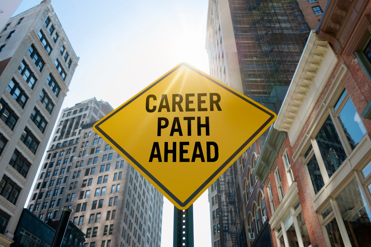 Yellow sign on a pole with the words "CAREER PATH AHEAD" written on it. Located in a city area.