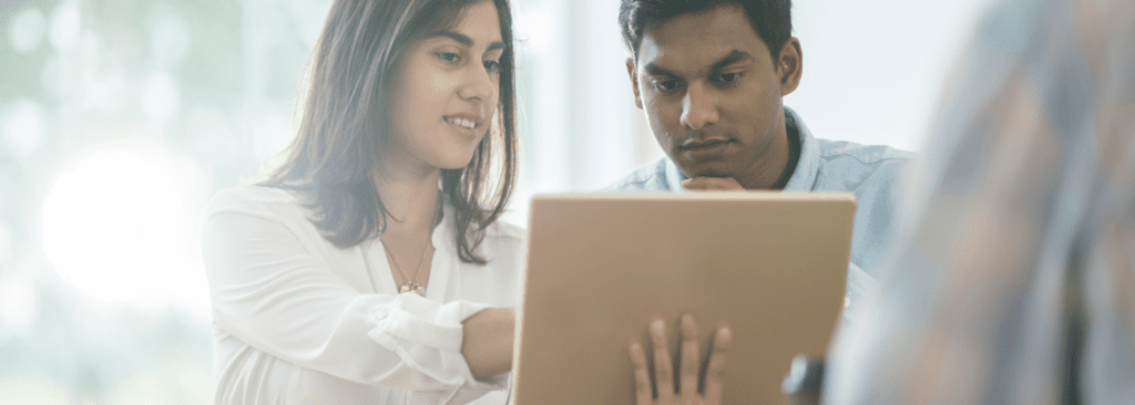 Two person is looking at a laptop as one person is pointing something towards it.