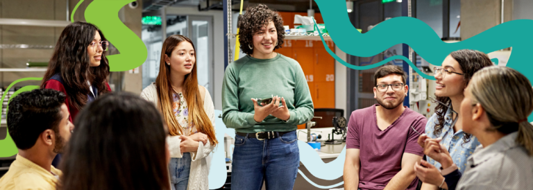 The image shows a group of 8 students standing in a room. They are wearing casual clothing, including jeans. Some of the people are smiling.