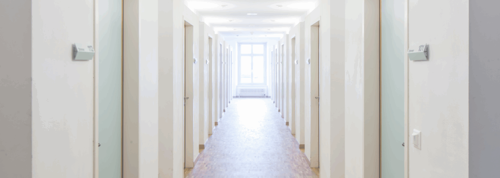 A hallway with a window at the end and closed doors along each side.