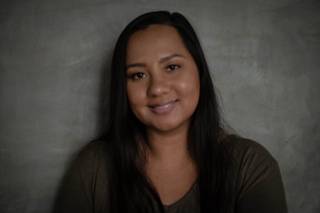 Smiling woman with long dark hair against a gray textured wall.