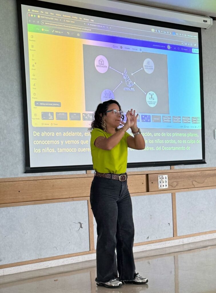 Zoé is wearing a bright green shirt with dark pants, signing in LSPR while presenting an APSSC slide covering education, rights and legislation, family and support, and accessibility and technology.