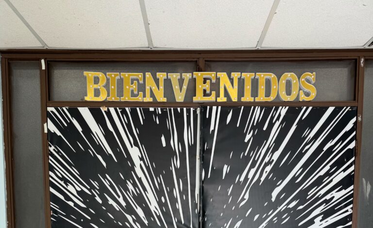A pair of double doors wrapped in a bold black-and-white starburst design, topped with gold marquee-style letters spelling "BIENVENIDOS.”