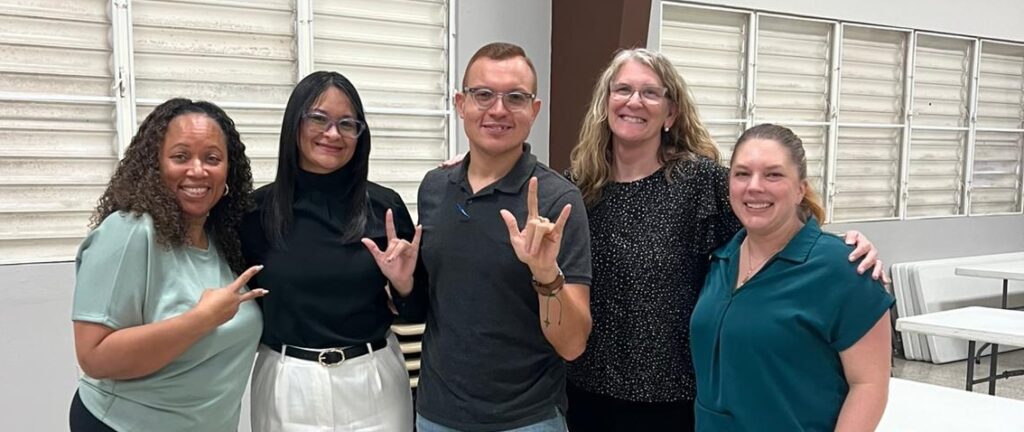 From left to right, Tia, Liz, César-Gabriel, Lore, and Kate - they are posed together indoors, smiling for the camera with two of them showing the "I love you" sign.